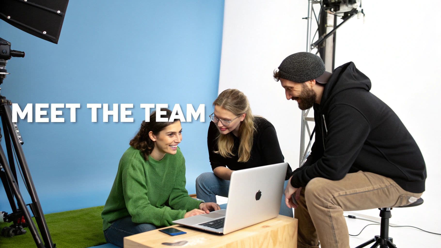 Equip creatiu somrient col·laborant en un portàtil en un estudi amb equip de càmeres.