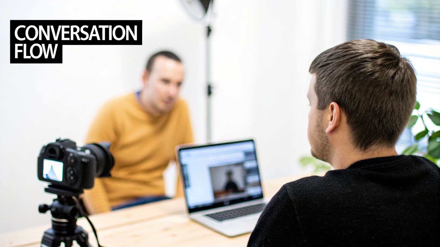 두 남성, 한 명은 카메라로 촬영당하고 다른 한 명은 'CONVERSATION FLOW' 텍스트가 있는 노트북을 사용하는 모습.